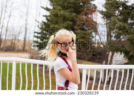 Young nerd girl with pigtails pushing up her black rimmed and taped glasses