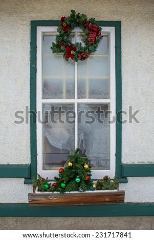 Tall frosted window decorated with Christmas wreath and small tree