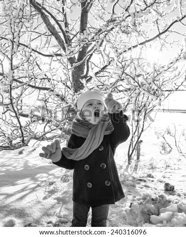 Toddler girl in peacoat and scarf posing by a frost covered tree in winter in black and white