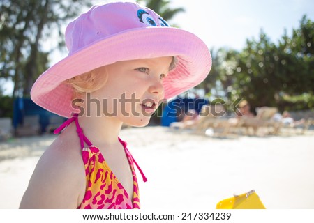 Upper body of little girl in swimsuit and floppy hat on a beach