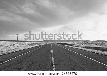 Close up of highway leading toward distant hills under cloudy sky in black and white