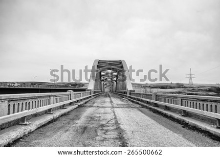 Decaying highway with guard rails leading to old abandoned arched bridge in black and white