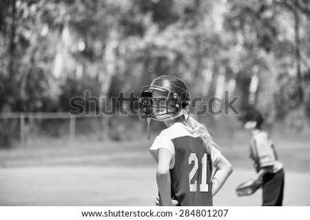 Upper body of A teenage girl in baseball helmet looking behind her in black and white