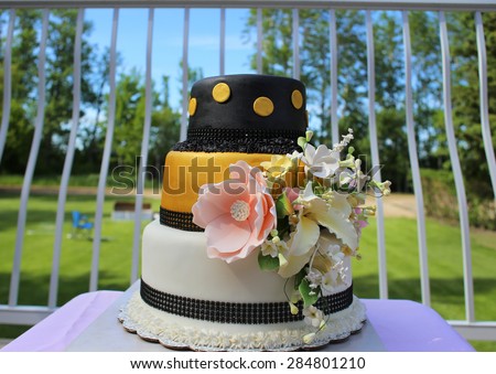 Three tier gold, black, and white wedding cake outdoors