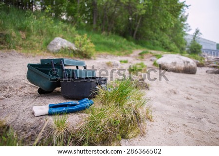 Fishing tackle box sitting on a sand beach with tufts of green grass