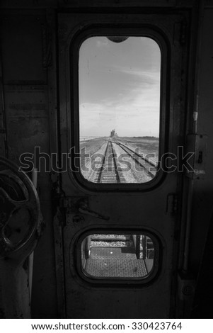 Railway track leading to a distant grain storage elevator framed by the interior dirty window of a railway car