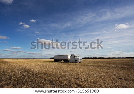 One white semi truck and trailer parked in a harvested field under dotted cloudy afternoon sky
