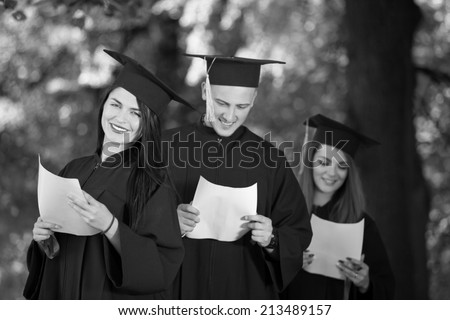 Portrait of happy students in graduation gowns holding diplomas on university campus