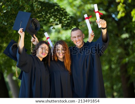 Portrait of happy students in graduation gowns holding diplomas on university campus