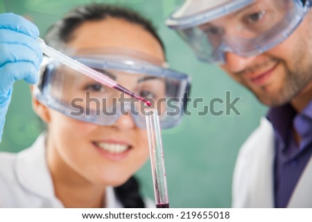 Attractive young female scientist and her male supervisor pipetting and microscoping in the life science research laboratory (biochemistry, genetics, forensics, microbiology..)