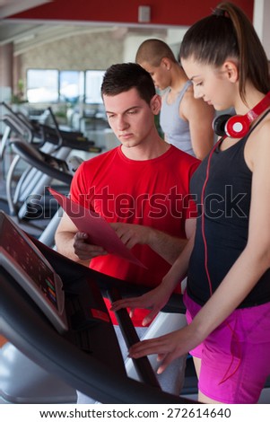 Trainer explains to a young woman how to use treadmill in fitness club