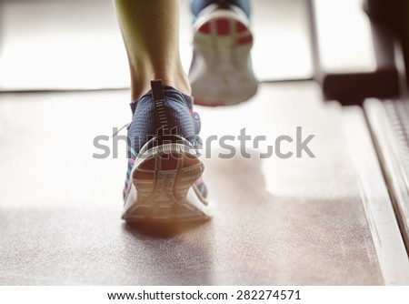 Fitness girl running on treadmill. Woman with muscular legs in modern gym