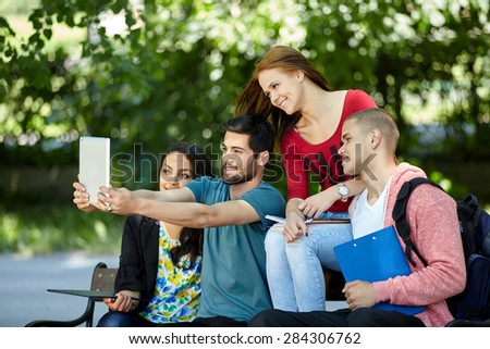 friendship, leisure, summer, technology and people concept - group of smiling friends making selfie with  tablet pc in park