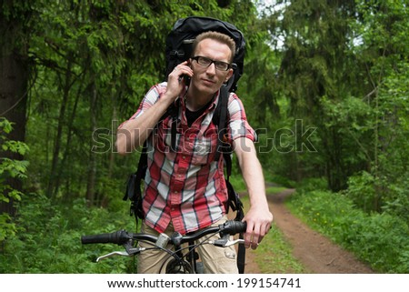 young man on a bicycle talking in the forest on a mobile phone. Modern communications everywhere.