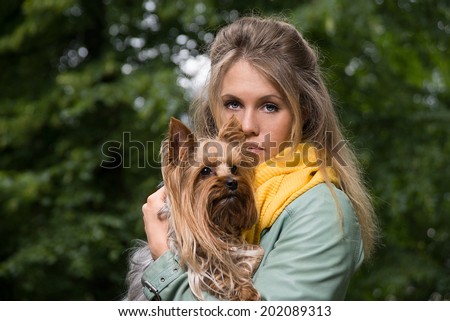 Young sad pretty blonde woman in city park. Small yorkshire terrier is on her hands. Concept animal care.
