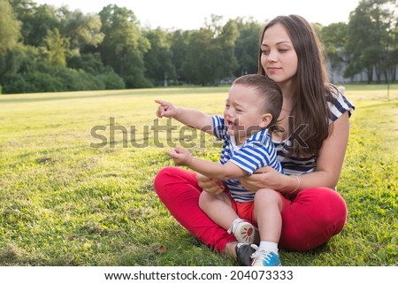 mother and child playing at the grass. naughty boy crying and and point by his finger. copy space left.