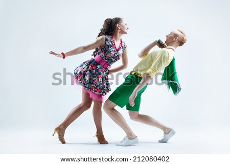 Funny dancer couple dressed in boogie-woogie rock\'n\'roll pin up style posing together in studio. Woman in yellow dress in black dots jokingly attack man in green shirt deviated from her.