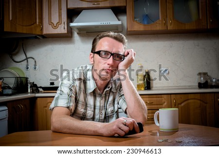 Frustrated man sits in the kitchen in front of a handful of coins and looks at the phone