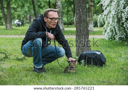 man playing the cat outdoor in summer day on cat's first walk