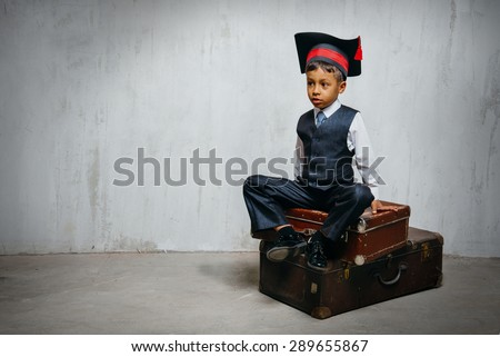 small black boy in suit and graduation hat sits on the old suitcases and look left. copy space left, instagram toned