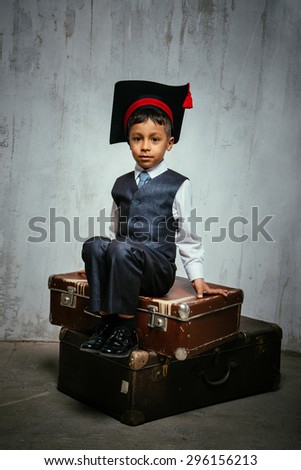 small black boy in suit and graduation hat sits on the old suitcases and look into the camera. instagram toned