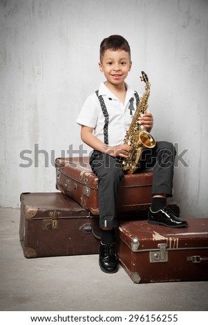 six years old boy sit with saxophone on old suitcases. instagram toned