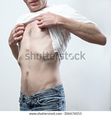 very thin man lift his t-shirt and looks for his chest.