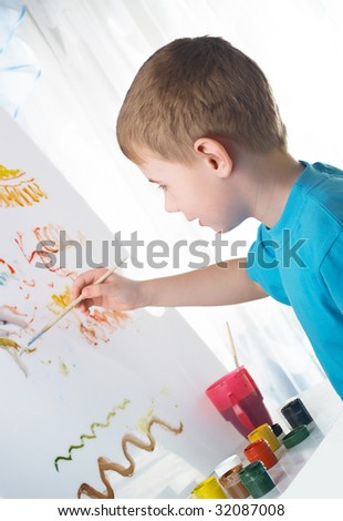 The boy draws with interest paints on a white cloth