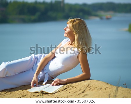 The girl reads the book on a beach on coast of the river