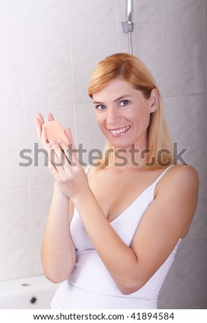 The young woman in a bathroom holds cosmetic means in hands