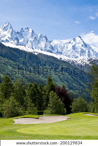 Golf field with sand bunkers over snow covered Alps.