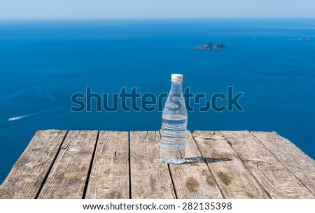 Bottle of fresh water on wood table over Mediterranean sea at the Pass of the Gods from Praiano to Positano at Amalfi Coast.