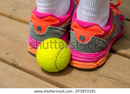 Children shoes and tennis ball on wood desk.