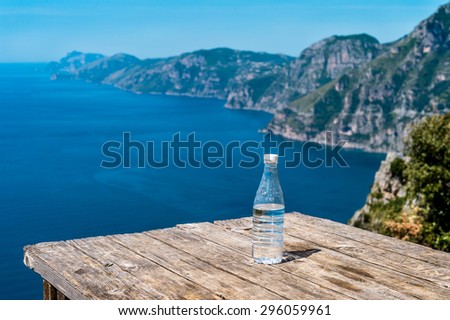 Water bottle on wood table at the hiking trail Pass of the Gods  over view of  Amalfi Coast.