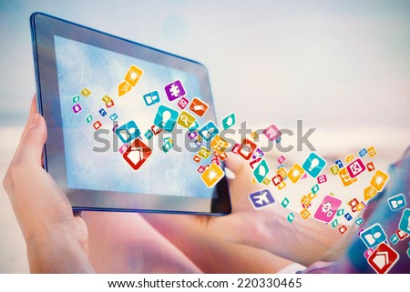 Woman sitting on beach in deck chair using tablet pc showing colourful computer applications