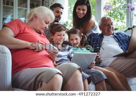 Happy multi-generation family sitting on sofa and using laptop, mobile phone and digital tablet