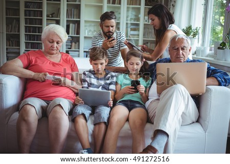 Multi-generation family sitting on sofa and using laptop, mobile phone and digital tablet
