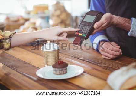 Customer entering pin number into machine at counter in cafe