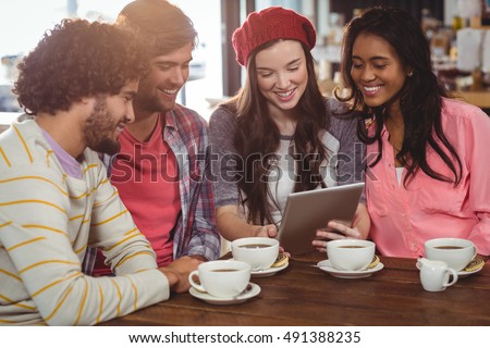 Group of friends using digital tablet while having cup of coffee in cafe