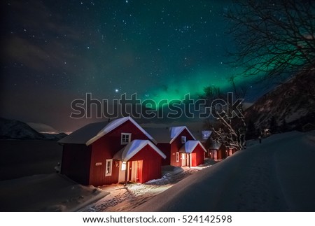 Northern lights (Aurora Borealis) over the red snowed-in cottages in Lapland village
