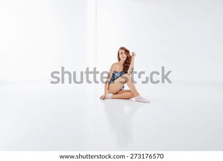 Beautiful girl sits on a glossy white floor in a white room, dressed her short blue suit, pink socks, her curly hair, beautiful eyebrows