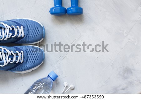 Flat lay sport shoes, bottle of water, dumbbells and earphones on gray concrete background. Concept healthy lifestyle, sport and diet. Focus is only on the sneakers. Sport equipment.