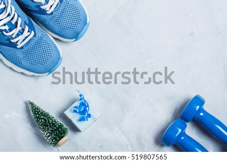Christmas sport flat lay composition with shoes, dumbbells, christmas tree and blue gift \
box on gray concrete background. Concept CÂ�hristmas special for healthy lifestyle and \
sport.