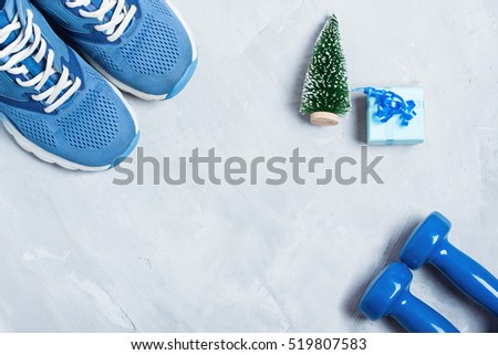 Christmas sport flat lay composition with shoes, dumbbells, christmas tree and blue gift \
box on gray concrete background. Concept CÂ�hristmas special for healthy lifestyle and \
sport.