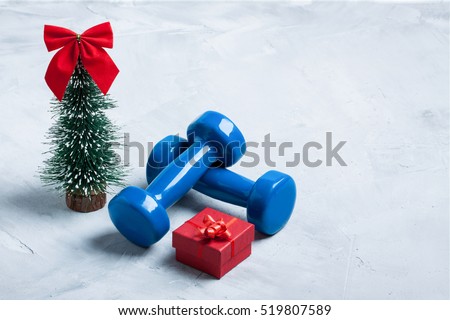 Christmas sport composition with dumbbells, red gift box and  christmas tree with red bow \
on gray concrete background. Concept CÂ�hristmas special for healthy lifestyle and sport.