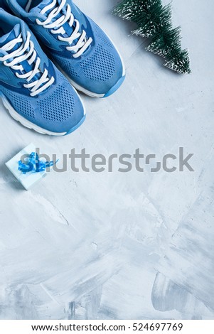 Christmas sport flat lay composition with shoes, christmas tree and blue gift box on gray concrete background. Concept christmas special for healthy lifestyle and sport. Vertical orientation