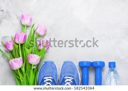 Spring flatlay sports composition with blue sneakers, dumbbells, bottle \
of water and purple tulips on gray concrete background. Concept healthy \
lifestyle, sport and diet in spring. Top view.