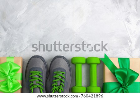 Holiday christmas birthday party sport flat lay composition with gray shoes, green dumbbells \
and craft gifts with green bow on gray concrete background. Top view, horizontal orientation