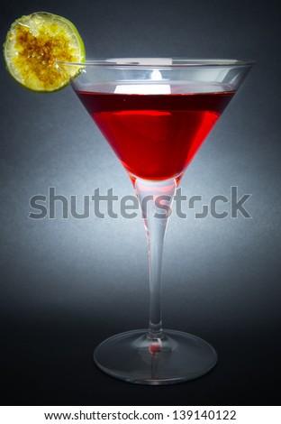 Cocktail made with white rum, red liquor and simple syrup and decorated with slice of caramelized lime, isolated on dark background.