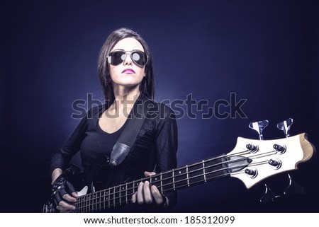 Young brunette woman playing bass against dark blue background, Music concept portrait
